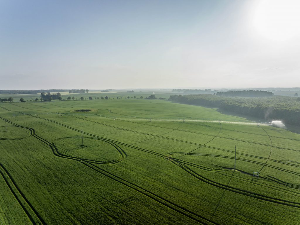Bild auf ein Feld auf dem eine verziehbaren Kreisberegnungsanlage gerade bewässert, aufgenommen von einer Drohne
